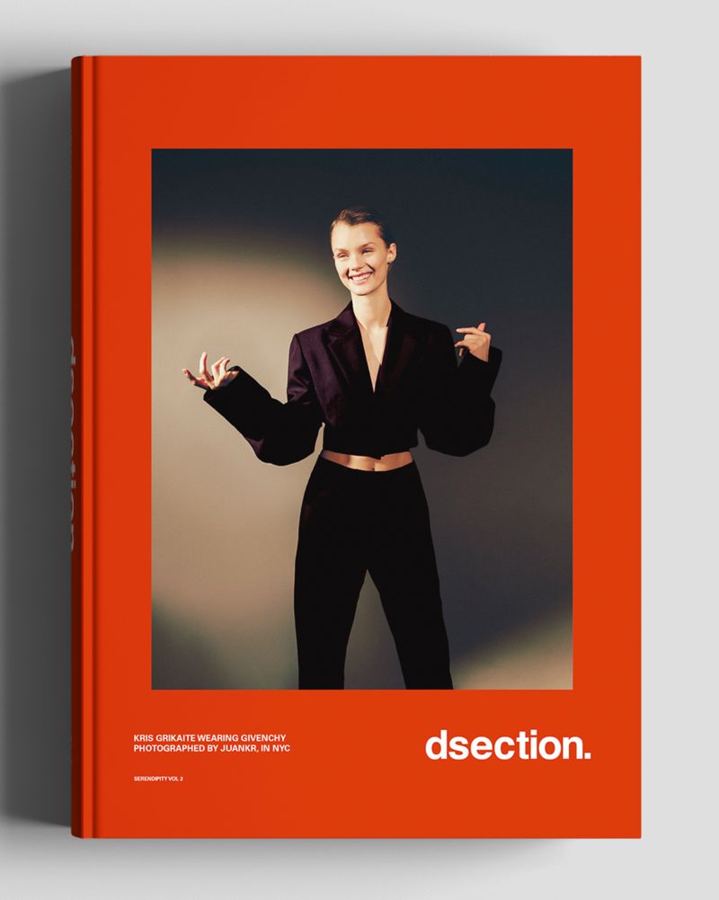 Book cover features a woman in a dark suit, smiling with hands raised on a solid grey background, cover is orange and title dsection.