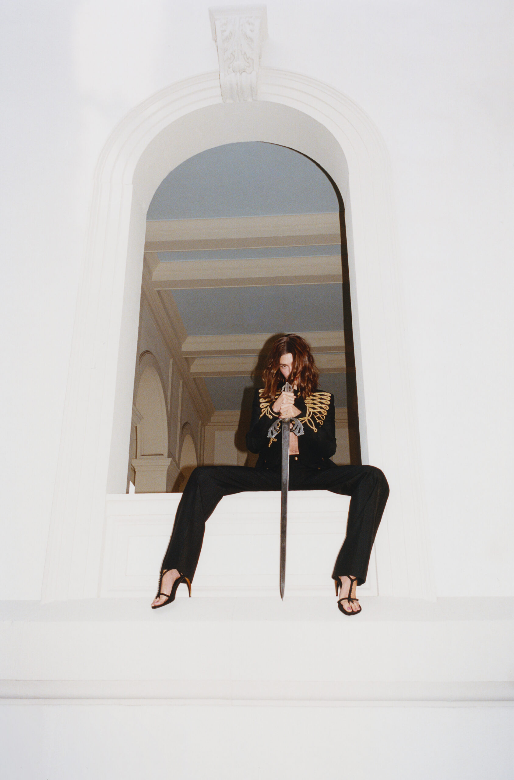 Model Hailey Bieber holding a sword while seated in an arched white window frame for Interview Magazine Spring 2026