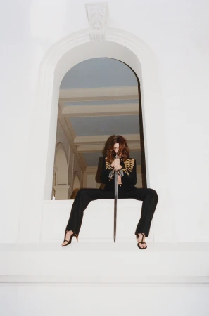 Model Hailey Bieber holding a sword while seated in an arched white window frame for Interview Magazine Spring 2026
