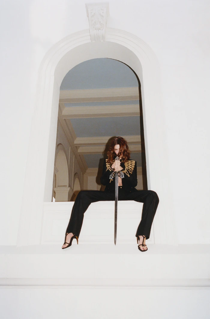 Model Hailey Bieber holding a sword while seated in an arched white window frame for Interview Magazine Spring 2026