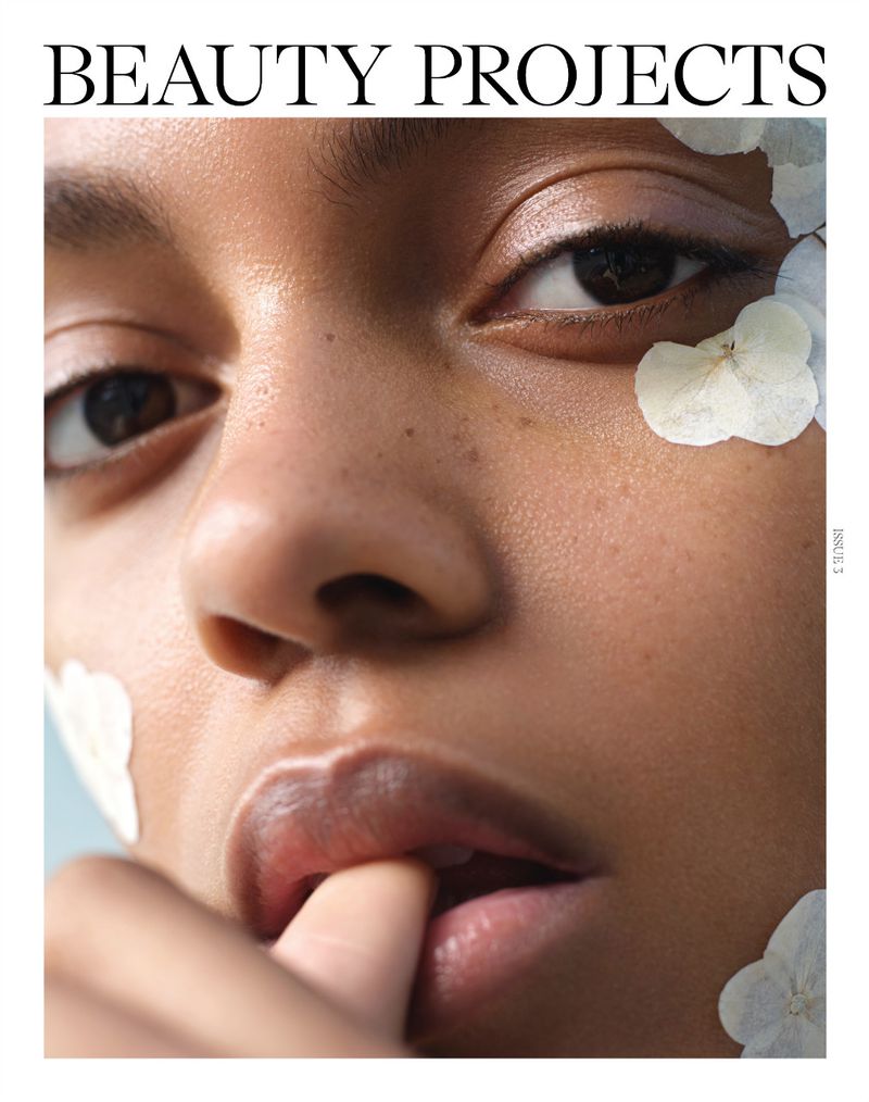 Close-up studio shot of a young adult female model with finger on lips, adorned with white flowers. Makeup and beauty concept.