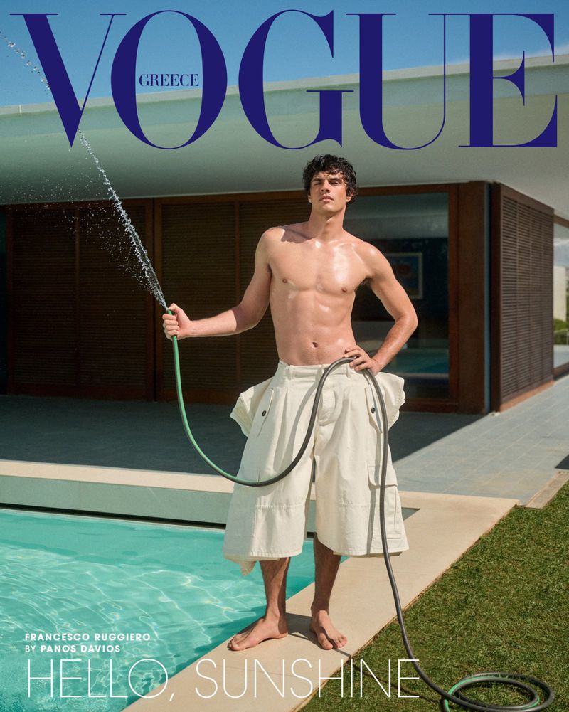 Vogue Greece cover featuring a shirtless adult male model outdoors, wearing white culottes, barefoot, watering the lawn with a green hose.