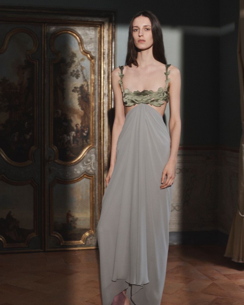 Model Saar Mansvelt Beck wearing a draped grey gown with sculpted green leaf bodice in an ornate interior for Valentino.