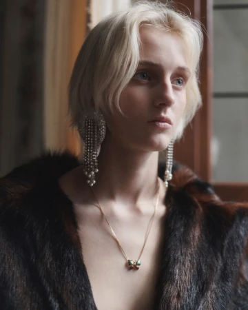 Model Saar Mansvelt Beck wearing a dark fur coat and long crystal chandelier earrings in soft window light for Valentino.