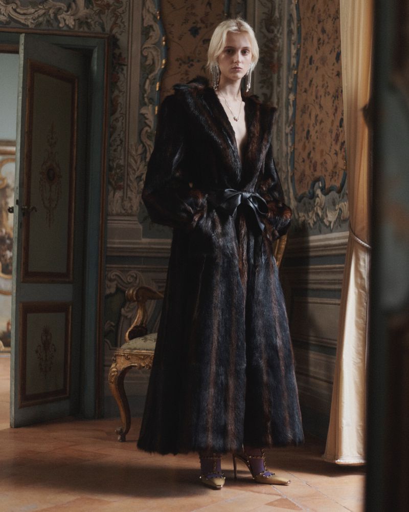 Model Saar Mansvelt Beck wearing a long dark fur coat with a tied waist belt in an ornate classical room for Valentino.
