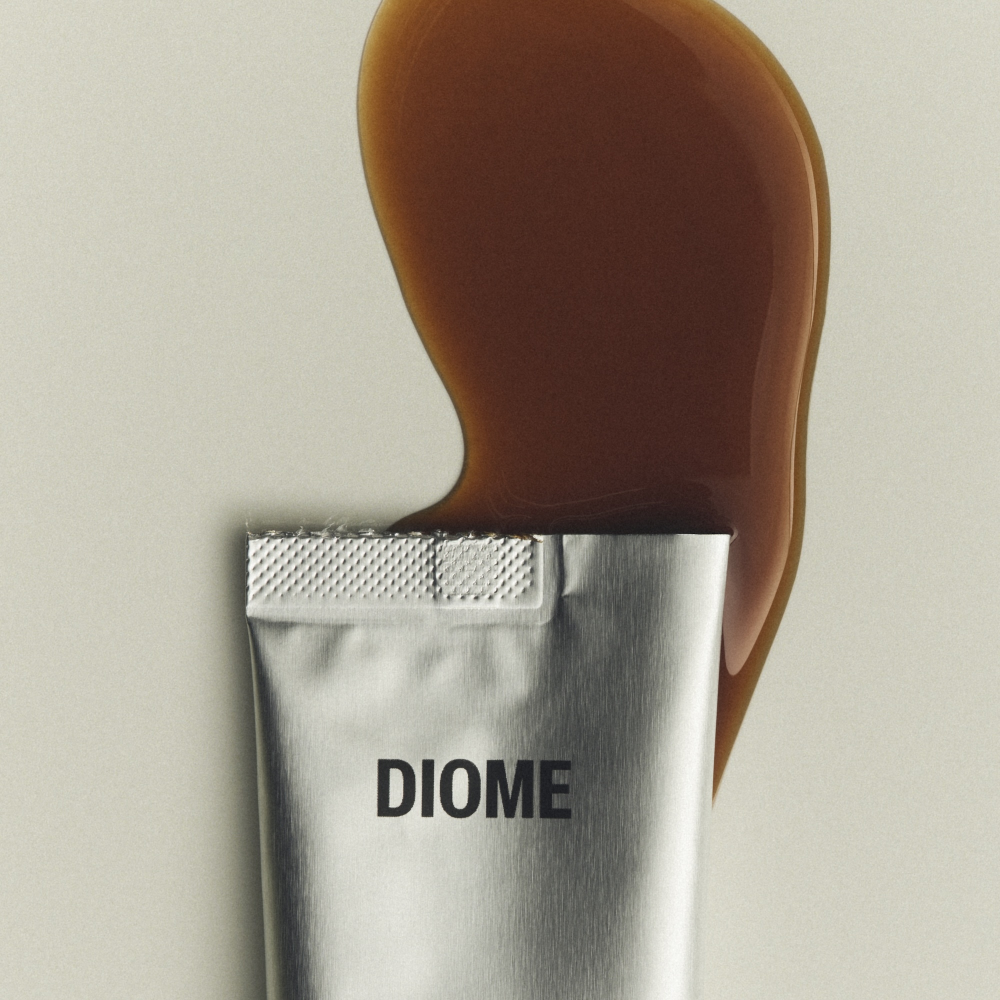 Silver aluminium cosmetic tube with black Diome logo beneath a glossy amber-brown liquid smear on a neutral grey background.