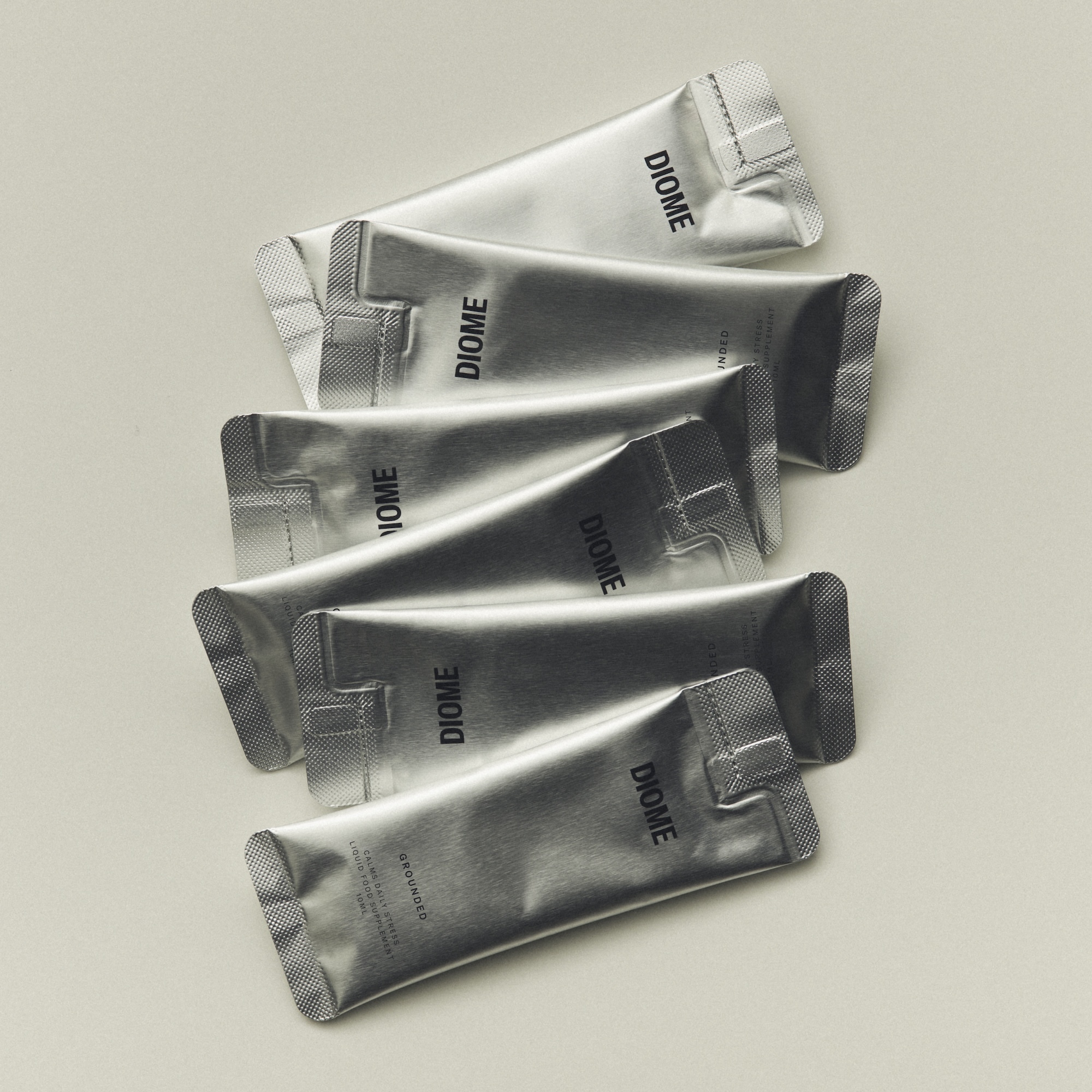 A staggered vertical stack of silver metallic foil packaging sachets printed with the Diome logo on a neutral off-white background.