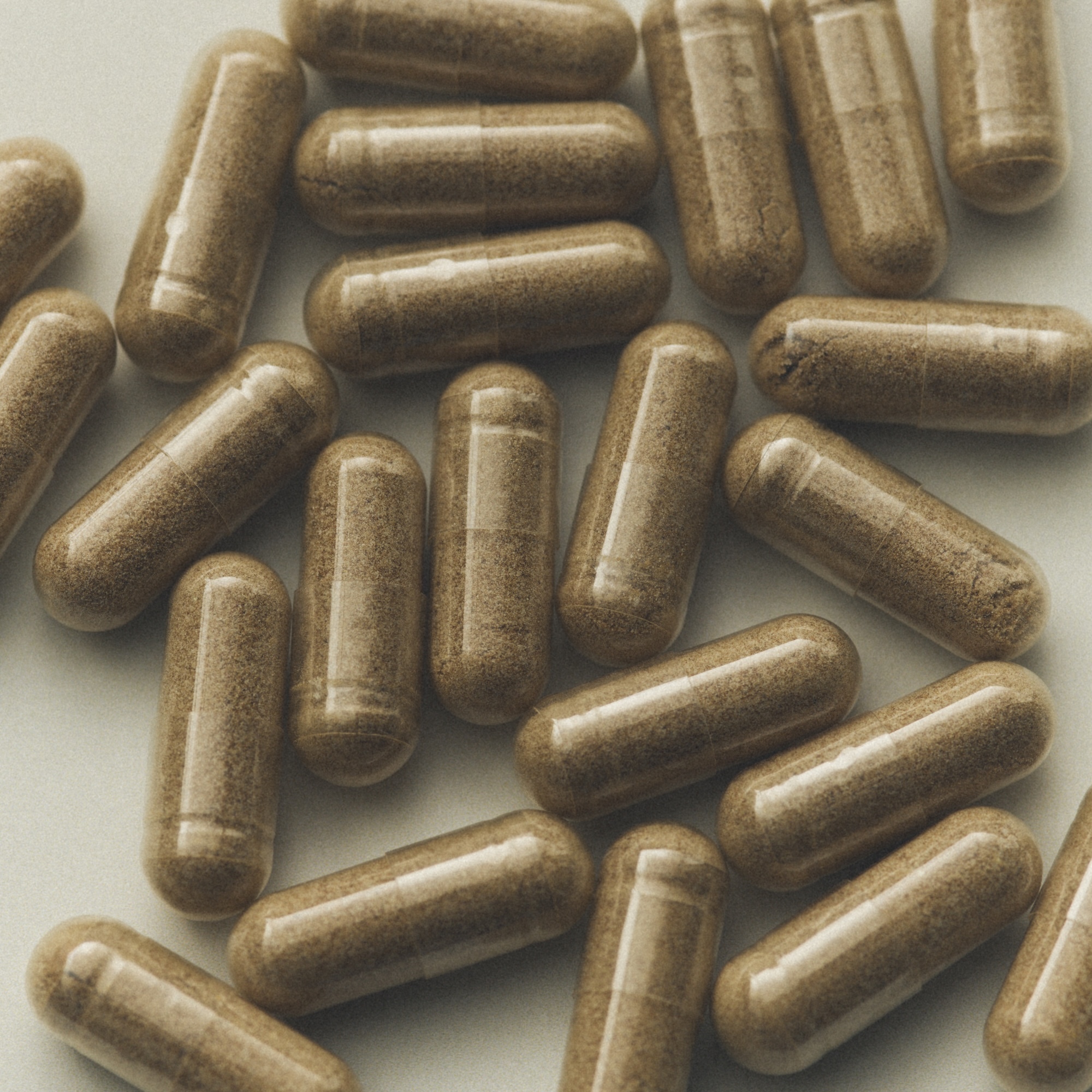 Close-up overhead view of clear supplement capsules filled with finely ground light brown herbal powder scattered on a neutral surface.