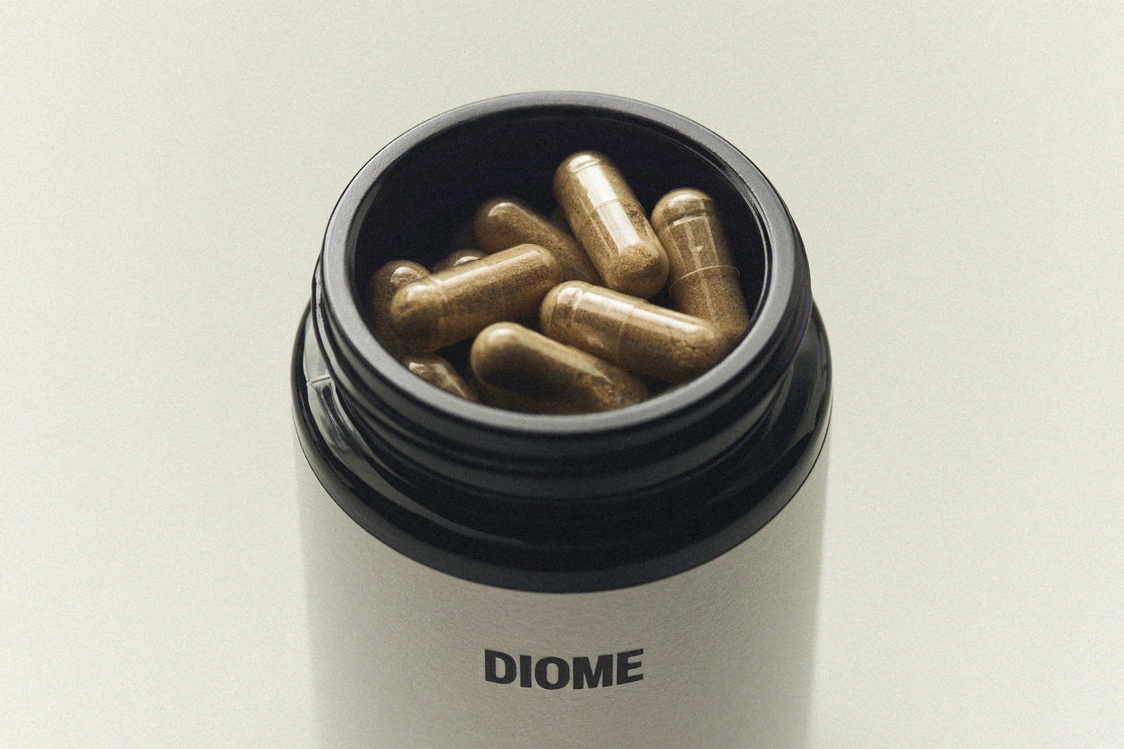 Top-down view of an open Diome bottle filled with transparent capsules containing brown powder against a plain background.