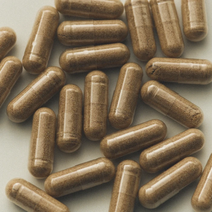 Close-up overhead view of clear supplement capsules filled with finely ground light brown herbal powder scattered on a neutral surface.