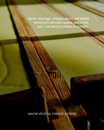 Cold-pressed artisanal soap slabs curing on slotted wooden drying racks with French descriptive text overlays.