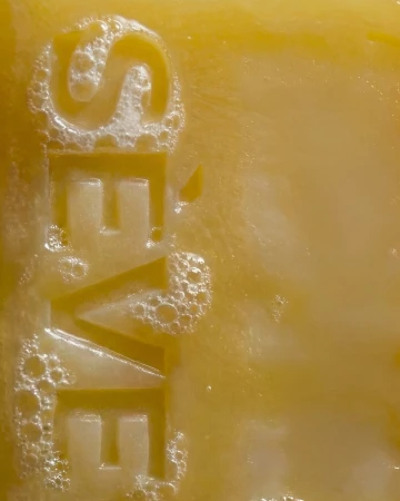 Extreme close up of a translucent yellow soap bar debossed with the word SEVE and covered with white soapy bubbles.