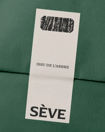 Rectangular off-white paper tag with black typography and SÈVE branding placed over textured dark green packaging paper.