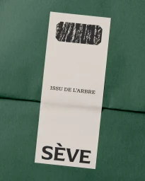 Rectangular off-white paper tag with black typography and SÈVE branding placed over textured dark green packaging paper.