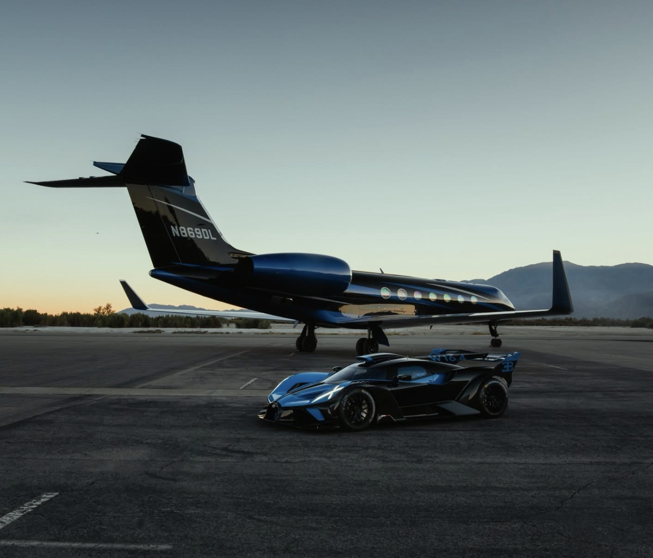 Bugatti Bolide sports car in black and blue parked on an airfield tarmac in front of a matching private jet at dusk.