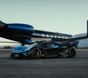 A blue and black Bugatti hypercar parked on an airport tarmac in front of a dark luxury private jet with mountains in the background.