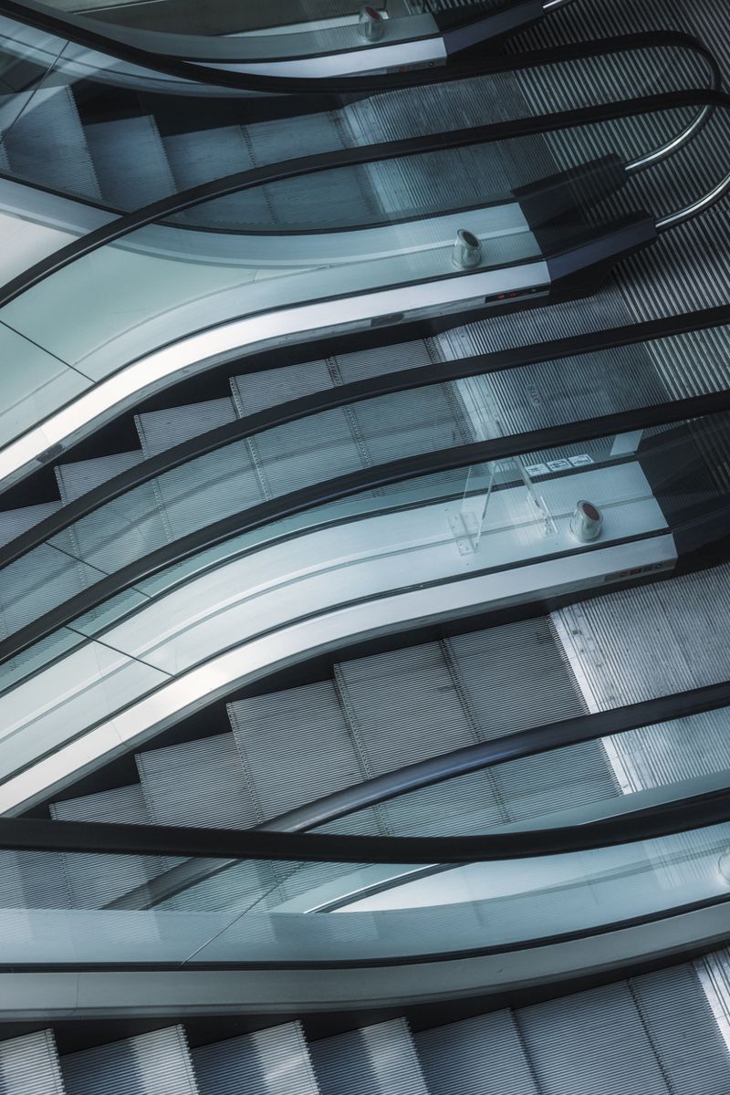 High-angle architectural view of modern crisscrossing escalators with glass panels, metallic steps, and dark curved handrails.