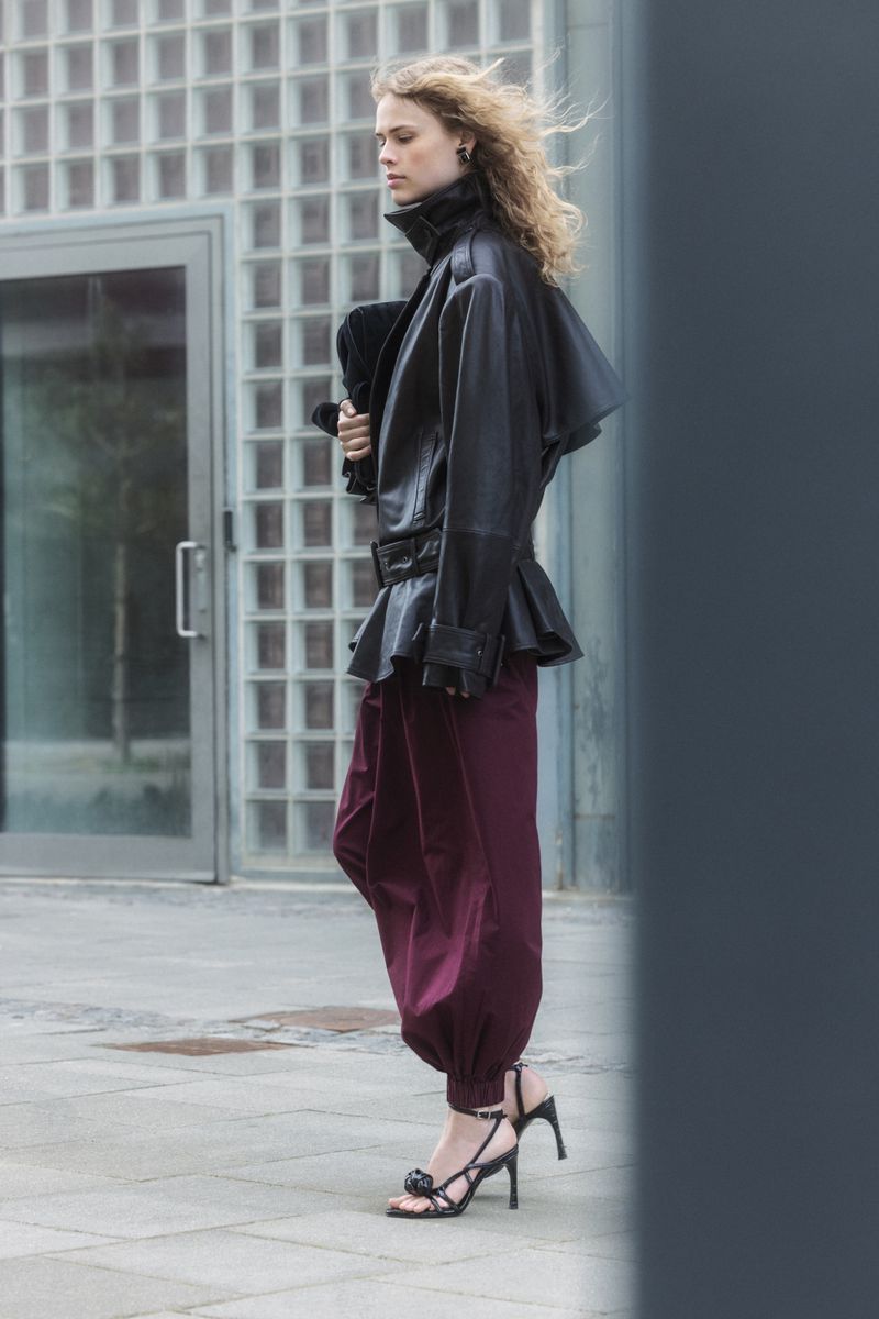 Model Tida Rosvall in a black leather belted jacket and burgundy harem trousers outdoors for the Rotate F/W 2026 campaign.