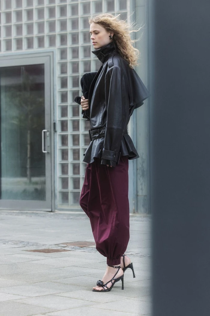 Model Tida Rosvall in a black leather belted jacket and burgundy harem trousers outdoors for the Rotate F/W 2026 campaign.