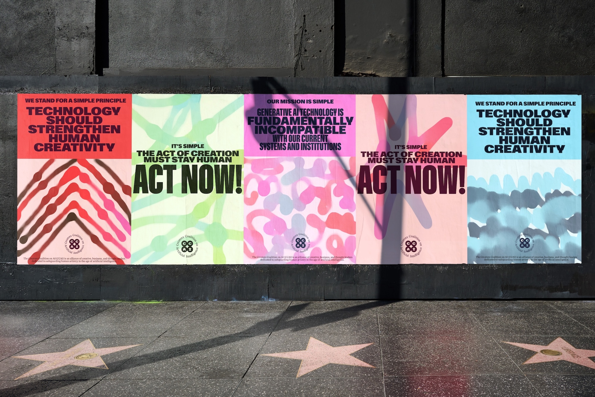 Five colourful typographic campaign posters advocating for human creativity pasted along a dark wall above a sidewalk.