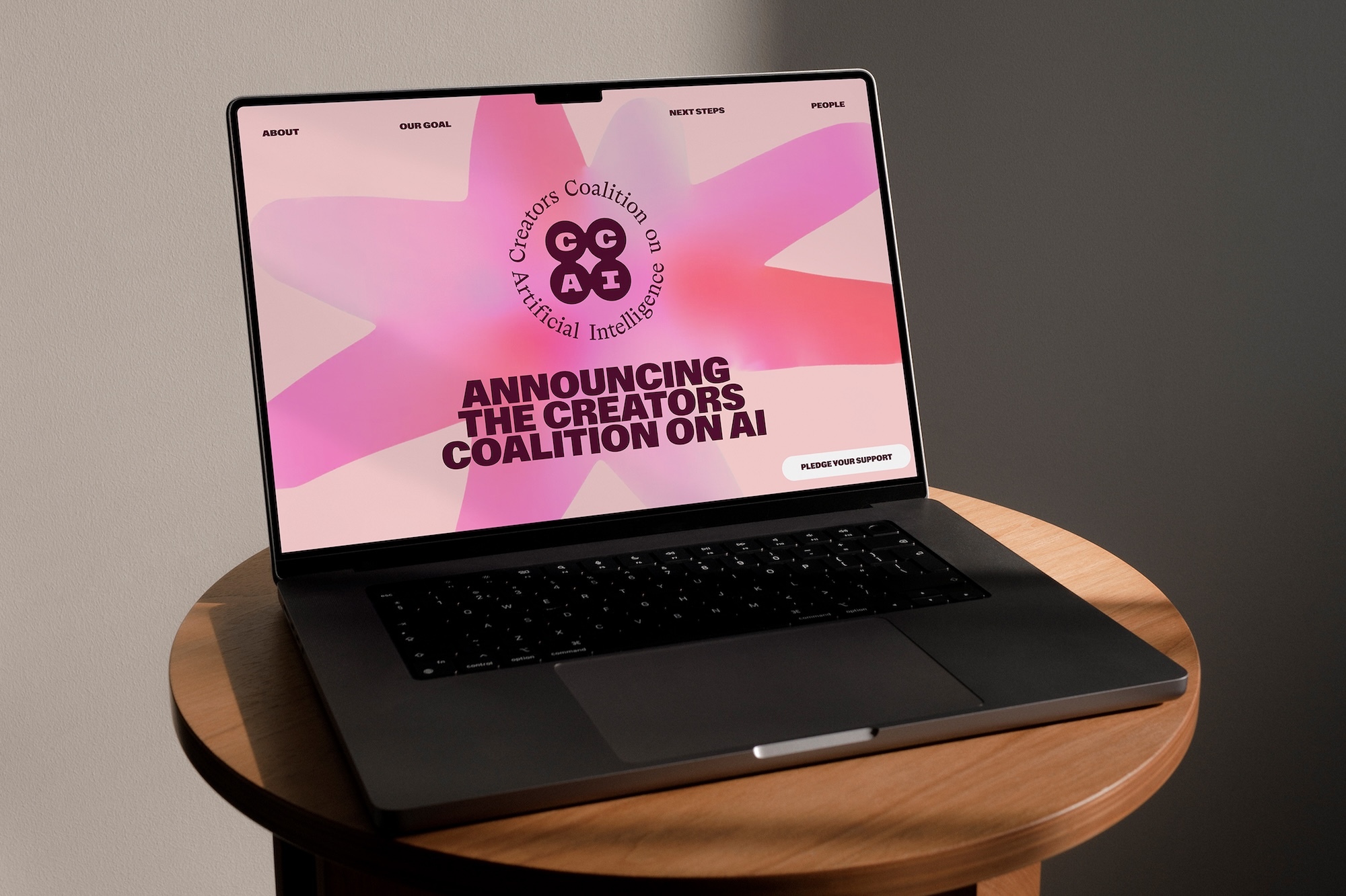 Dark laptop on a round wooden table displaying the Creators Coalition on AI website with pink graphic artwork on screen.