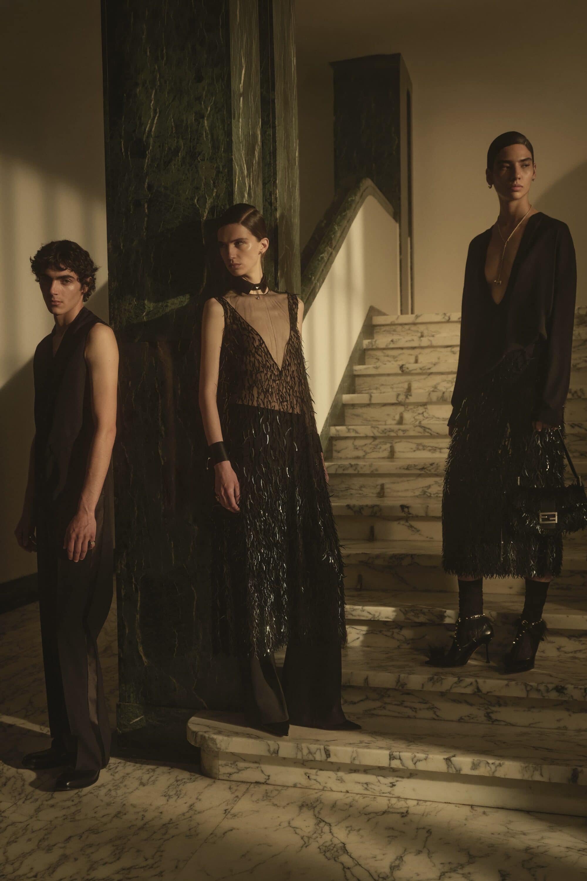 Three models posing on marble stairs inside a grand interior with dramatic low lighting for a Fendi campaign