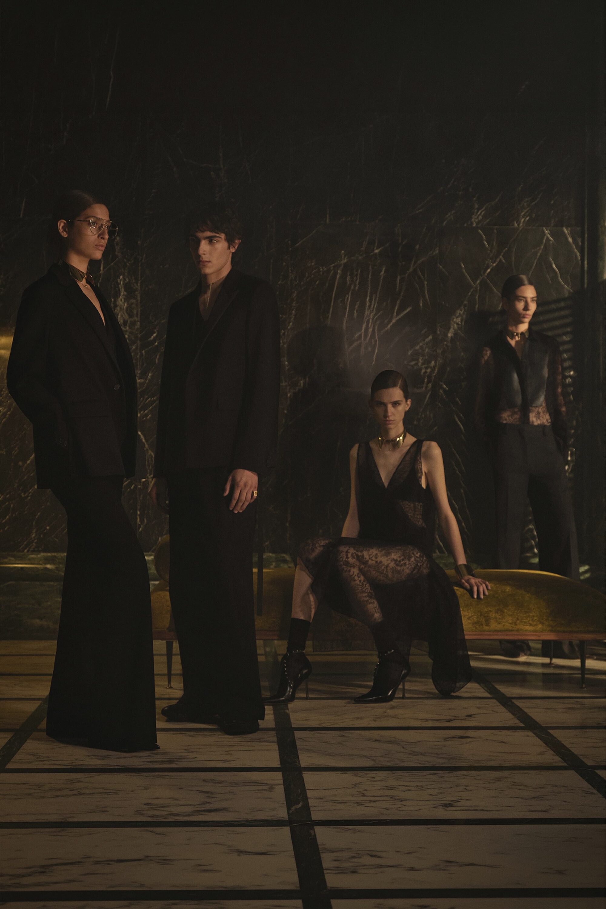Four models dressed in black tailoring and eveningwear posing in a dimly lit room with a grid floor for Fendi.
