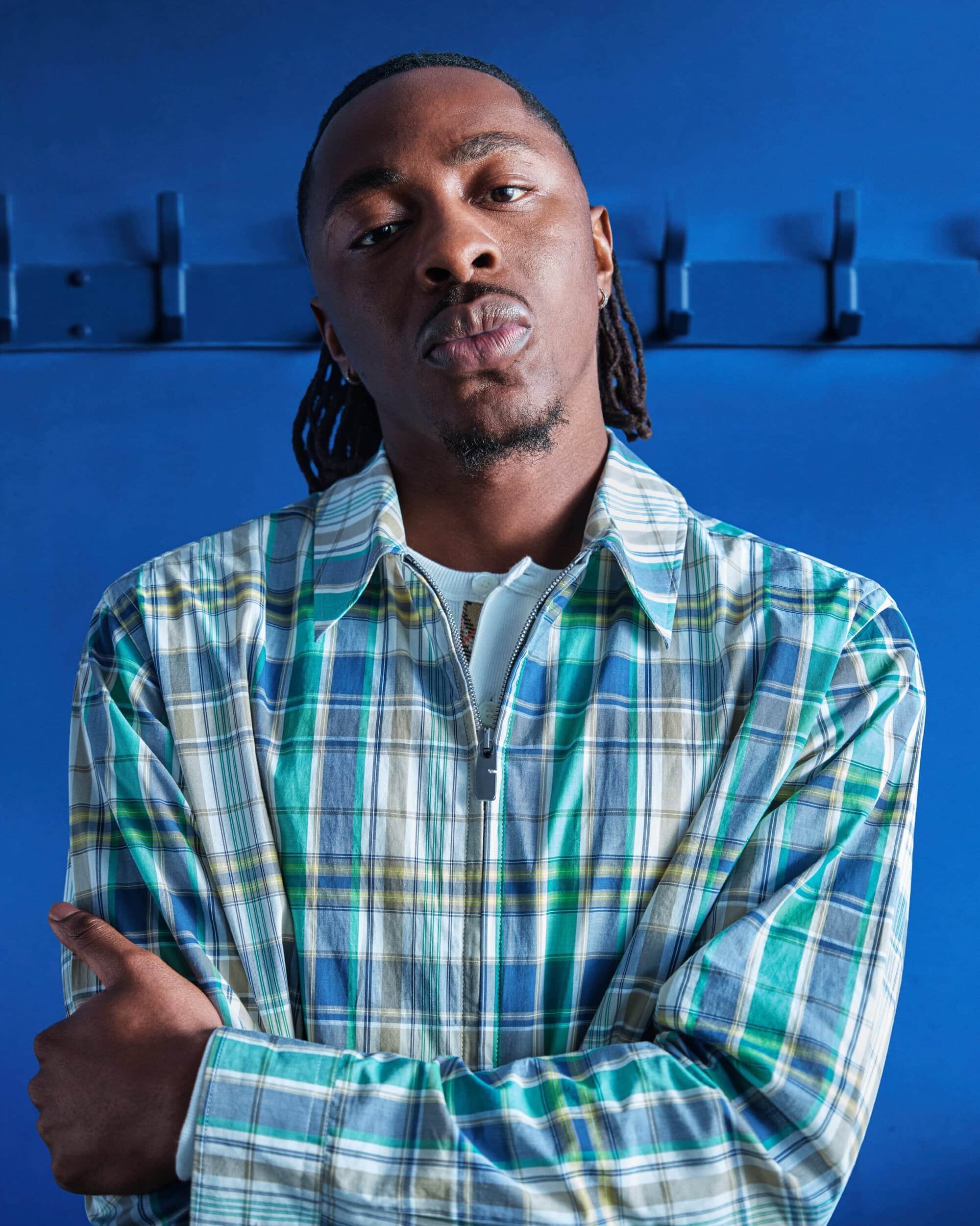 Eberechi Eze wearing a green and blue plaid zip jacket with arms crossed against a blue background for Burberry.