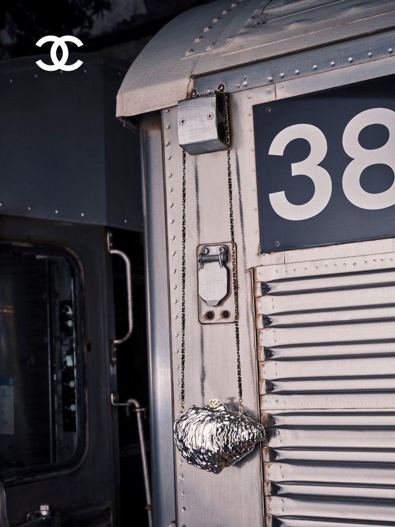 Chanel metallic oyster shell clutch hanging from a chain strap against the corrugated metal exterior of a train carriage.