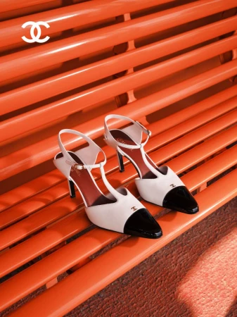 Chanel two-tone white and black T-strap slingback heels displayed on a bright orange slatted bench.