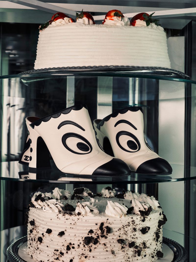 Chanel cartoon eye graphic heeled mules displayed on a glass shelf between frosted layer cakes.