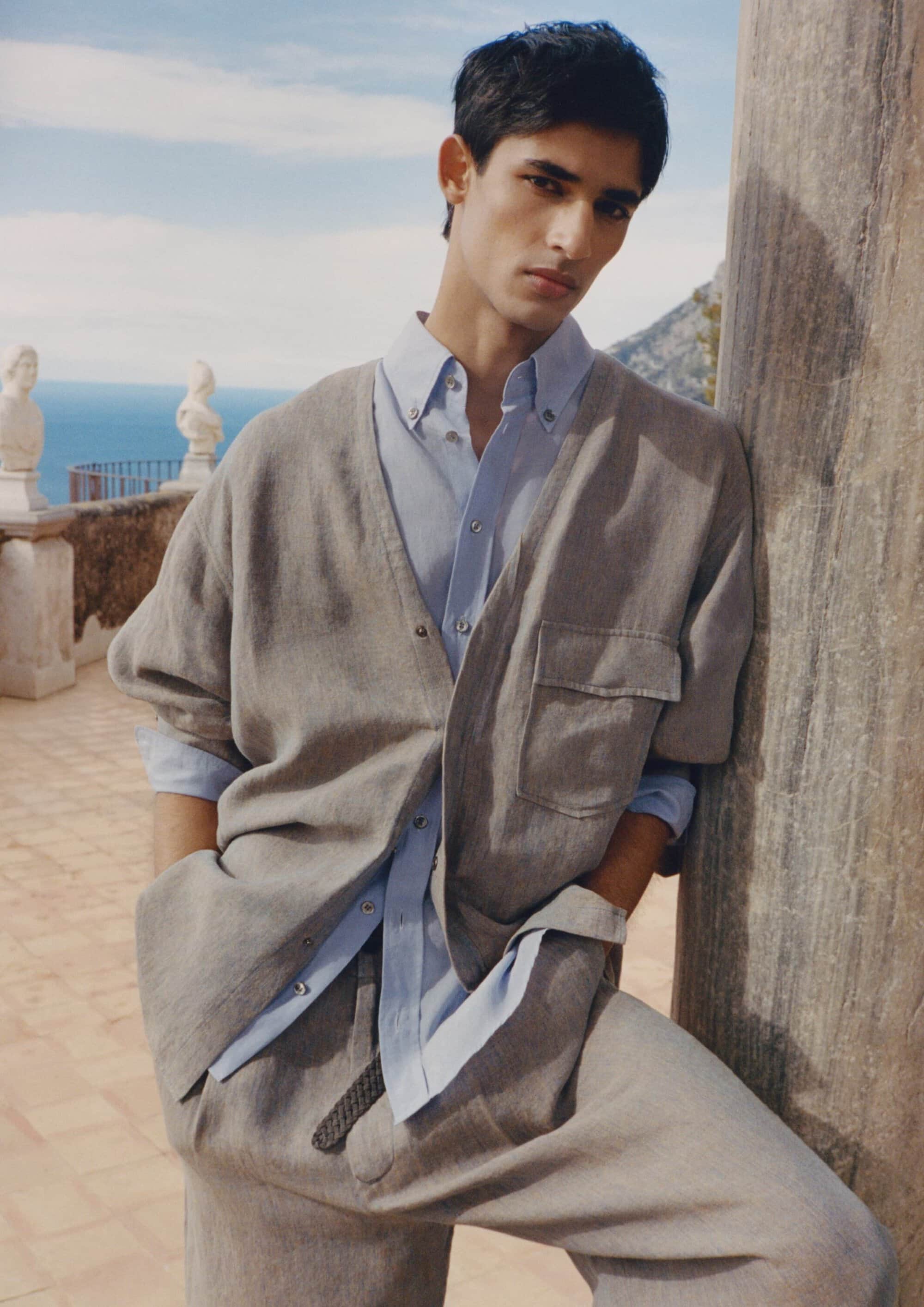 Model leaning against a stone column outdoors overlooking the sea in an ad campaign for Giorgio Armani.