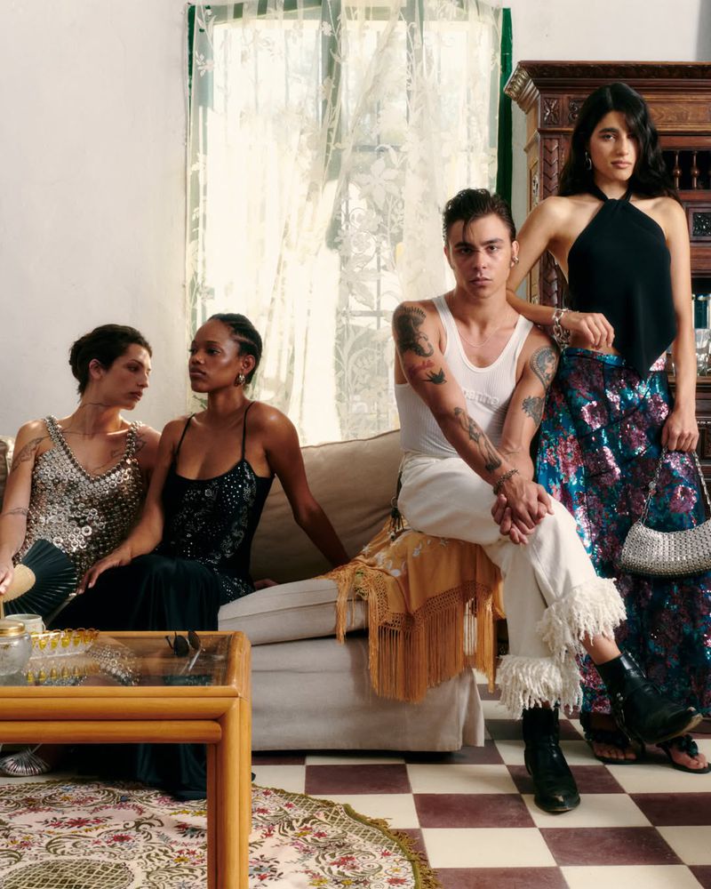 Four fashion models posing in an eclectic sunlit living room wearing Rabanne metallic tops, fringe trousers, and patterned skirts.
