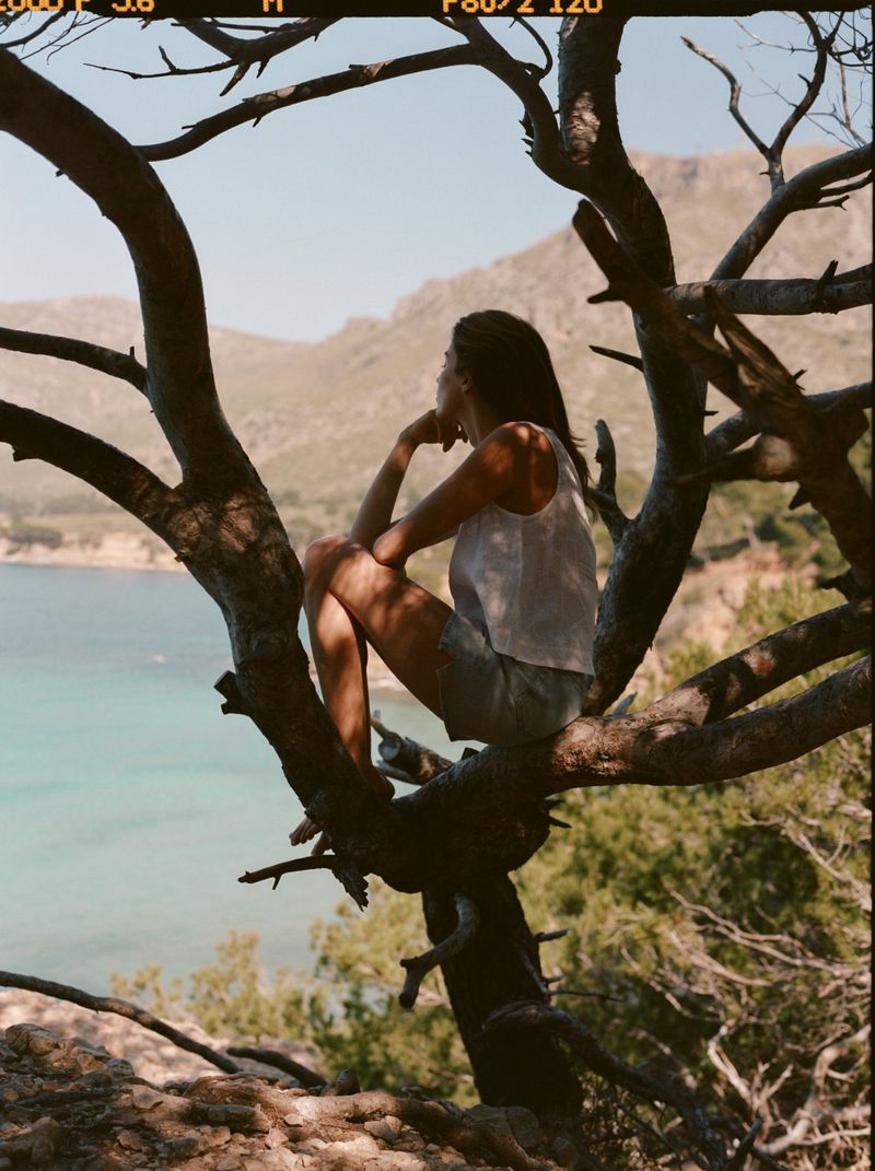 Constanze Saemann seated in a gnarled pine tree overlooking a coastal bay for Mavi Women's Summer 2026