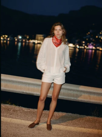 Constanze Saemann standing by a roadside barrier at night wearing a white blouse, white shorts, and a red neck bandana.