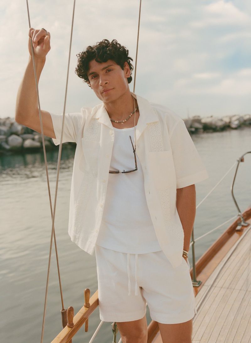 Hitesh Bisht wearing a white short-sleeve shirt and matching shorts on a sailboat deck for Abercrombie & Fitch.