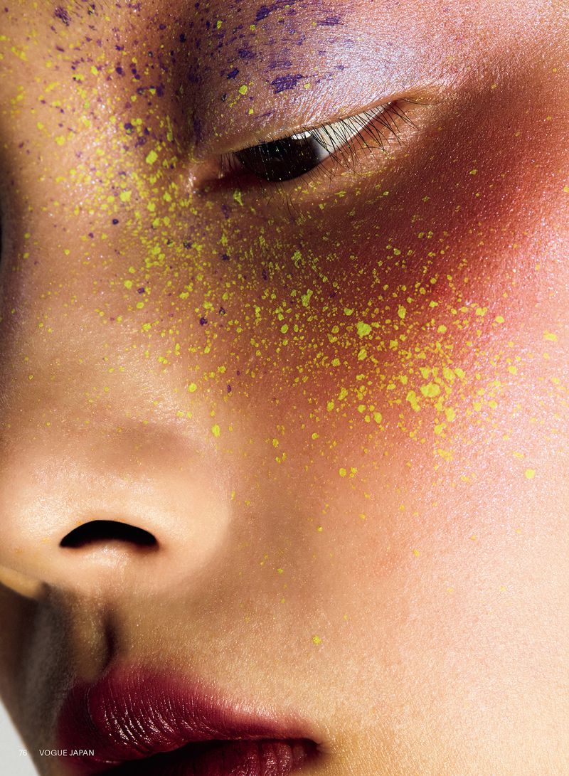 Extreme close-up of a woman's face featuring yellow speckled pigment, blended red blush, and deep berry lipstick.