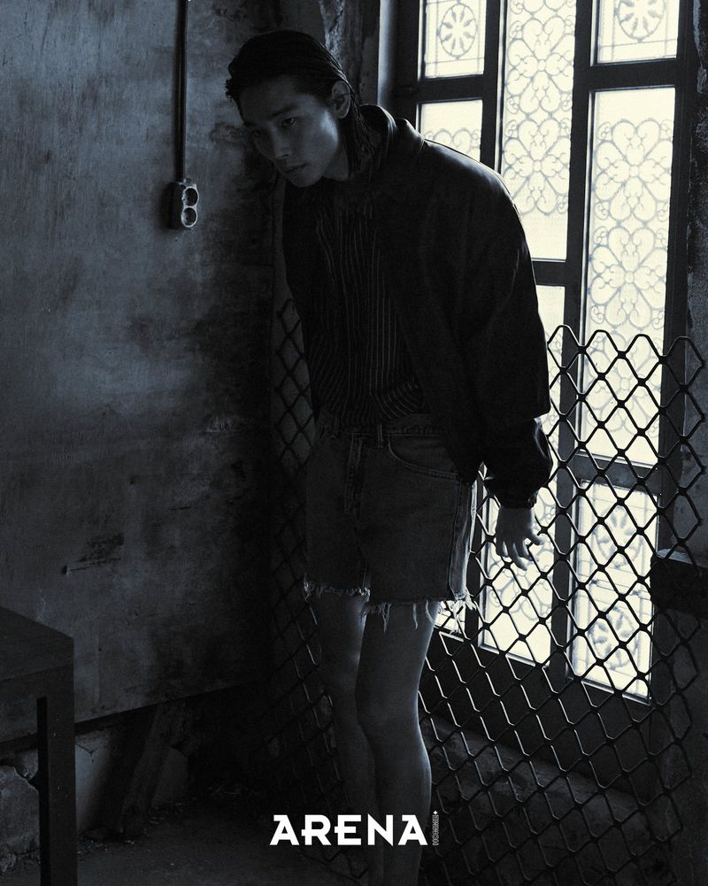 Model Taemin Park stands beside a mesh-covered window in a dark jacket, striped shirt, and frayed denim shorts.