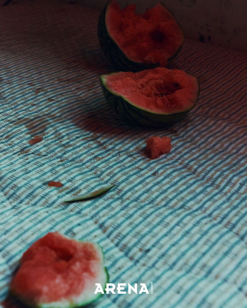 Eaten pieces of watermelon with red flesh resting on a striped fabric mat with juice stains.