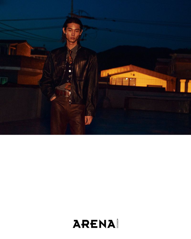 Model Taemin Park wearing a black leather jacket and brown trousers on a rooftop at dusk for Arena Homme+ Korea.