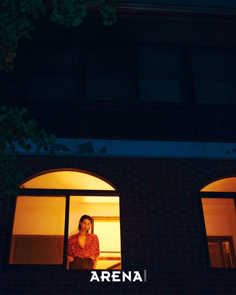 Model Taemin Park standing in an illuminated window of a brick building at night for Arena Homme Plus Korea