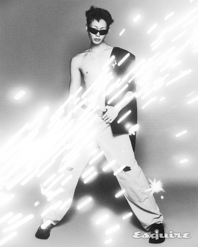 Model Minki Kwon posing shirtless with a draped blazer, sunglasses, and trousers amidst glowing diagonal light streaks for Esquire Korea.