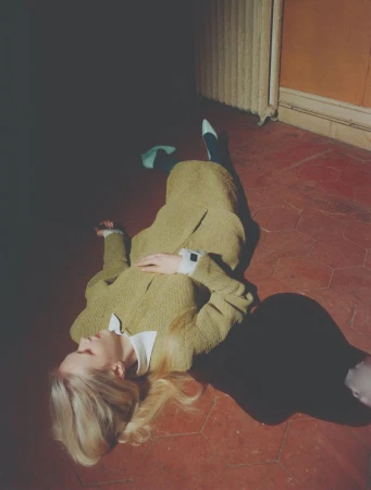 Model lying on red tiled floor wearing yellow knit dress with white collar and heels