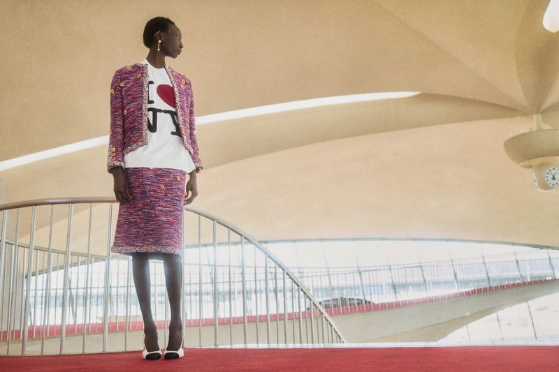 Woman in pink tweed skirt suit and white 'I love NY' t-shirt standing on red carpet, architectural background, high fashion editorial.
