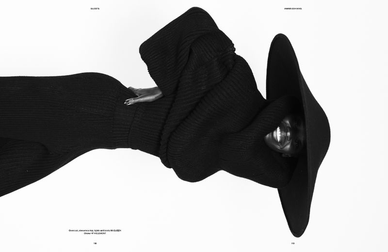 Model Awar Odhiang smiling while wearing a sculptural black knit sweater and wide-brim hat against a pure white background.