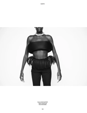 Black and white fashion portrait of model Awar Odhiang wearing a sculptural black bandeau and fringed waistpiece on a white background.