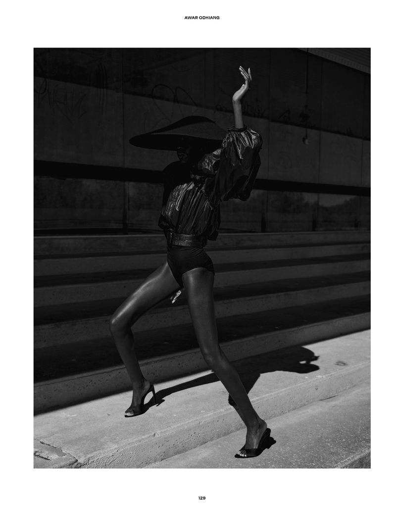 Model Awar Odhiang in a wide-brimmed hat and dark outfit posing outdoors on concrete steps for The Travel Almanac.