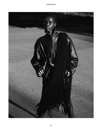 Awar Odhiang posing in a high-collar leather jacket with cascading braided tassels in a black and white fashion editorial.