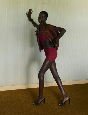 Model Awar Odhiang leaning against a pale paneled wall wearing a brown jacket and red romper by Vito Fernicola for The Travel Almanac.
