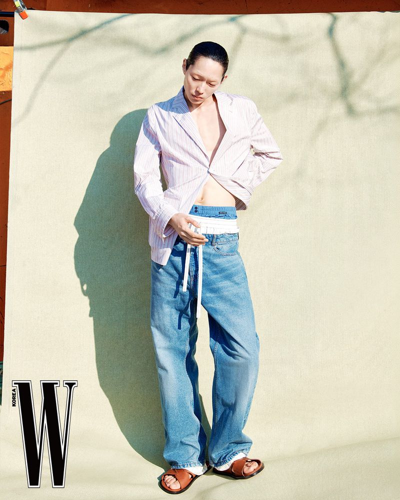 Model Minki Kwon wearing an unbuttoned striped blazer, layered wide-leg denim jeans, and brown sandals in a W Korea editorial.